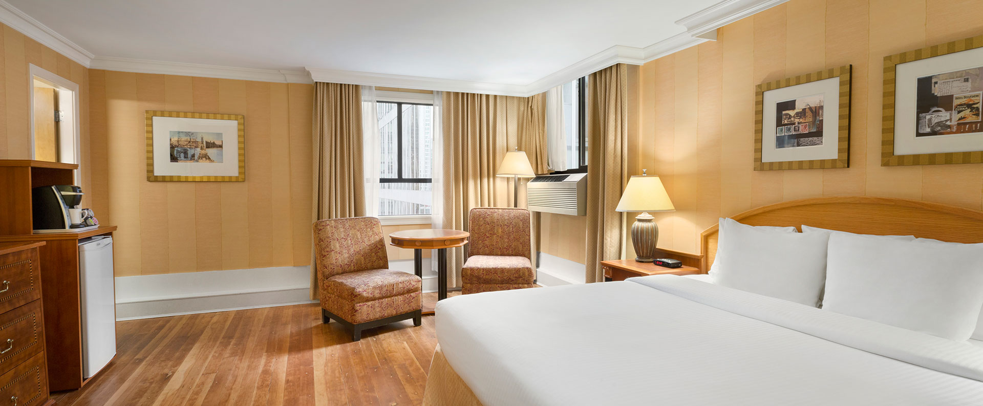 The Standard Queen room at Days Inn Vancouver Downtown features hardwood floors, comfortable chairs and tables arranged in a sitting area by the window and an air conditioner.